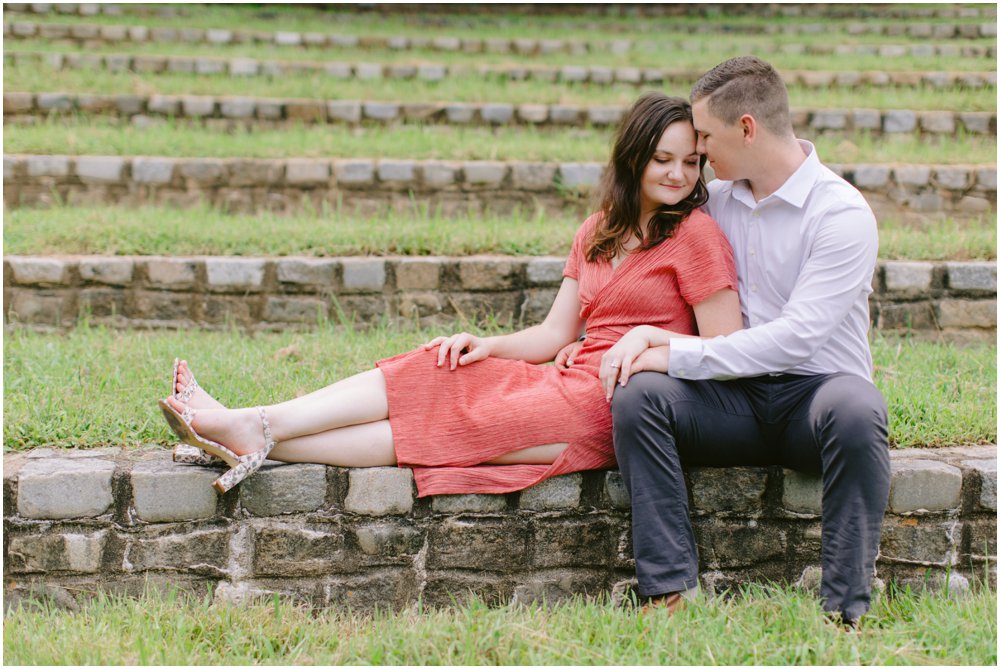 A woman leans into her fiancé for their park engagement photos