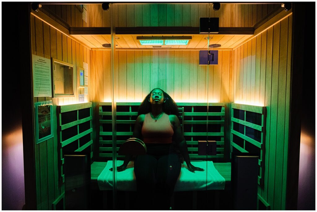 Women with orange top and eyes closed enjoying green light therapy in a sauna. 