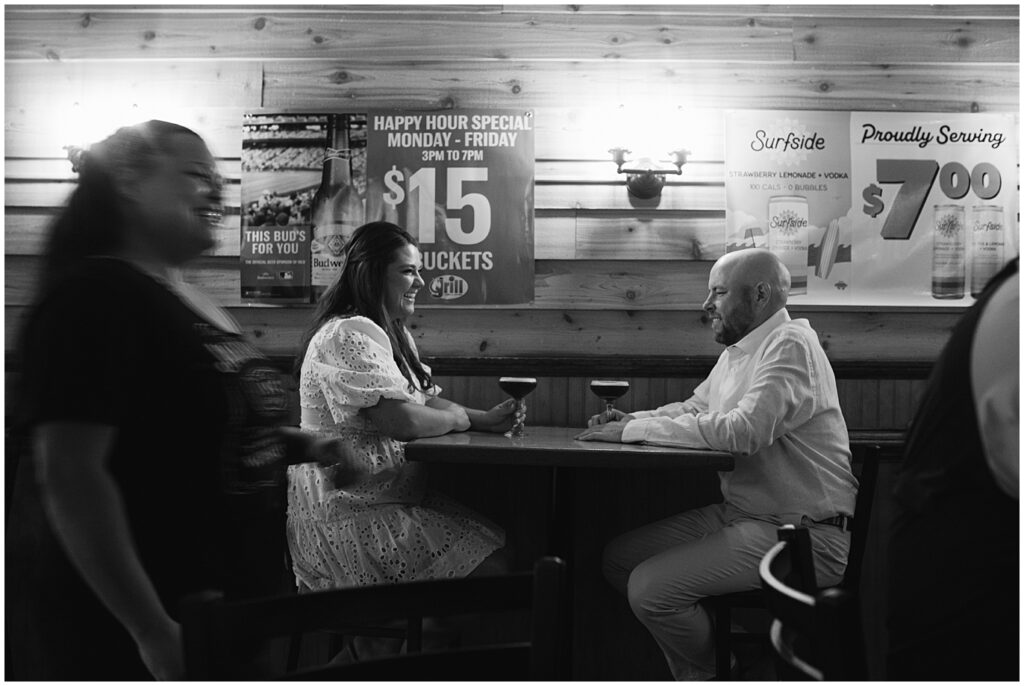 Couple sitting in a bar at their summer engagement session drinking drinks