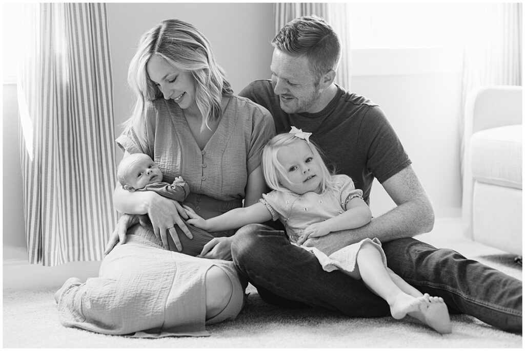 This is a picture of a mom becoming a mother of two. A mom is staring at her newborn son while being held by her husband and daughter.