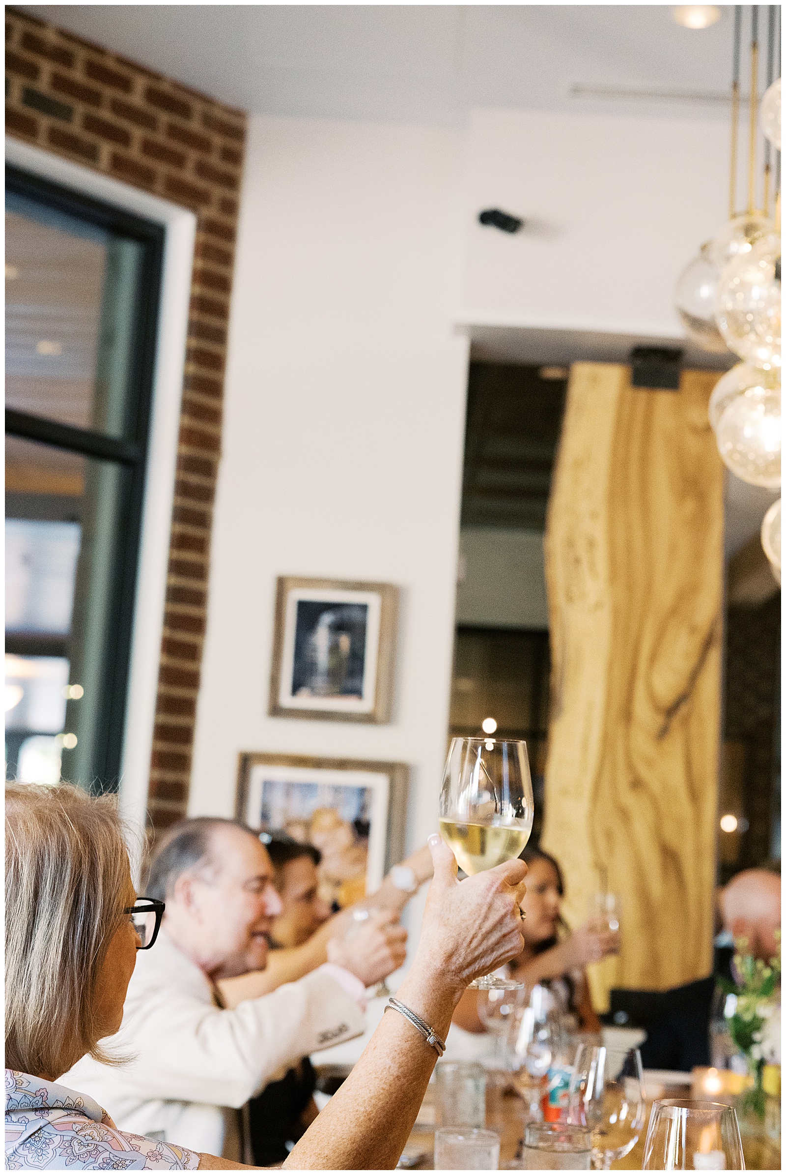 Woman holding up a glass of white wine doing a cheers at Shagbark restaurant in Richmond, Virginia.