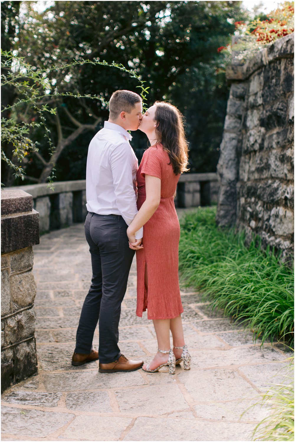 An engaged couple kisses on a stony park path