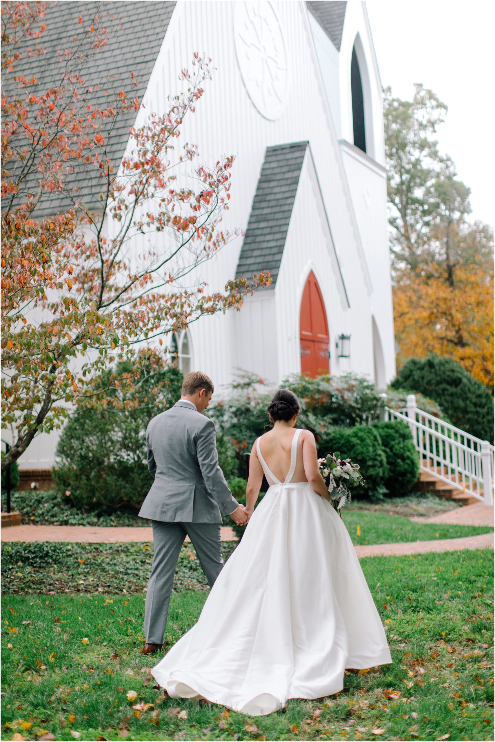 A couple walks to the church for their wedding on a fall day with leaves under their feet